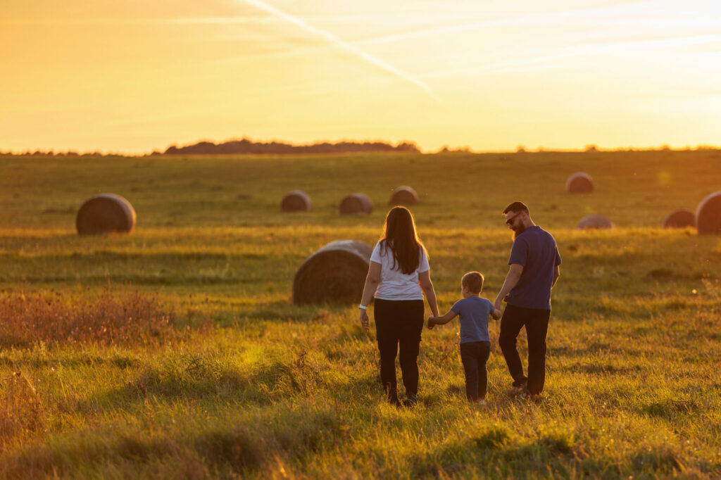 Mother, father and son are walking hand in hand through the wide fields of Lithuania in the evening light. A harmonious family during a walk in the fresh air